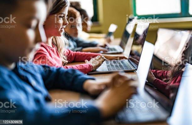 Happy schoolgirl and her classmates e-learning over laptops during a class in the classroom.